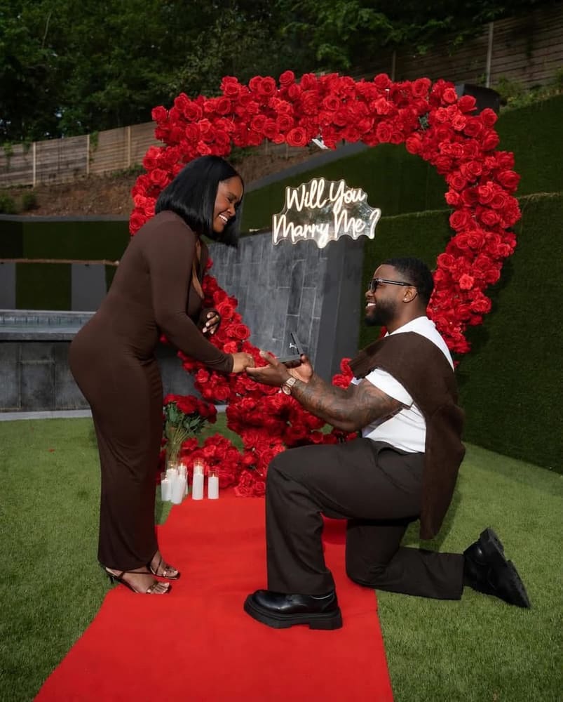 Marriage proposal on one knee at a red rose heart arch, red carpet underfoot