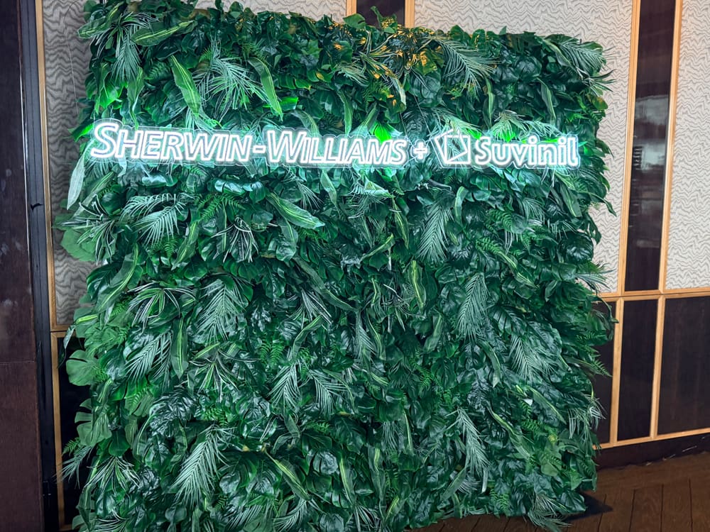 Greenery wall carrying a lit Sherwin-Williams and Suvinil brand sign
