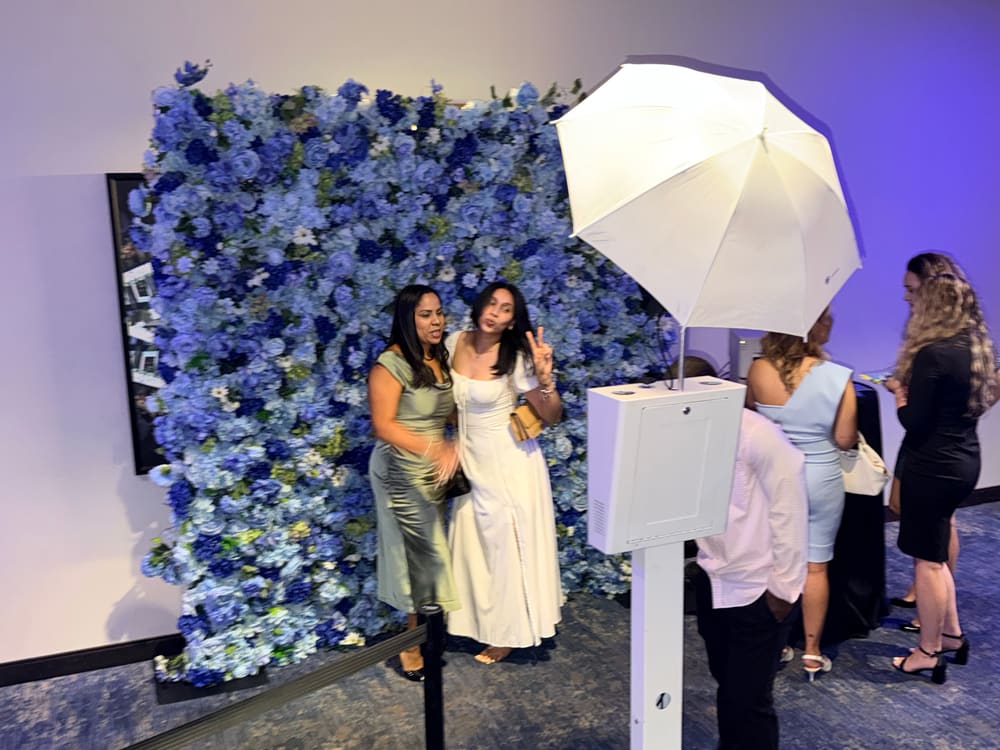 Guests posing together at a blue hydrangea wall beside a photo booth