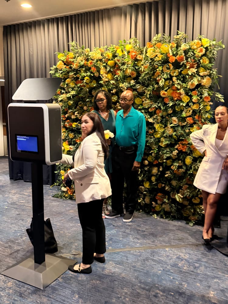 Guests queueing at a photo booth in front of a yellow and orange rose wall