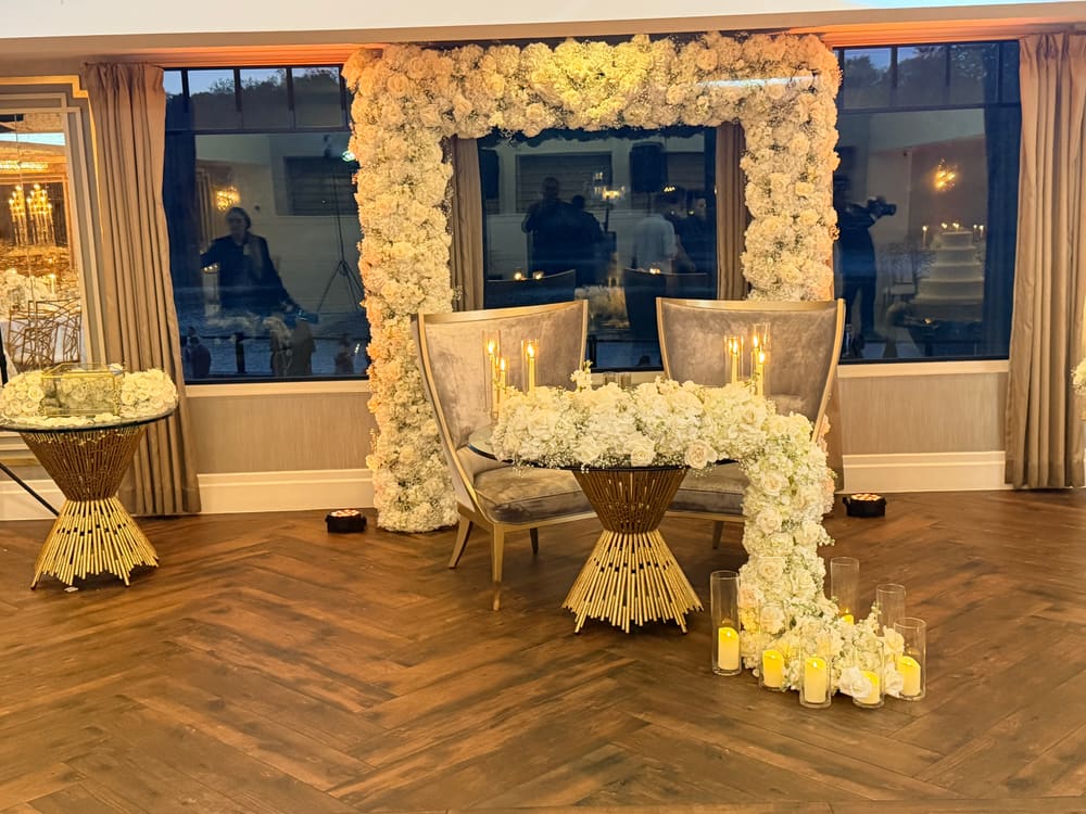Ivory floral arch framing a window, with chairs and candlelight beneath